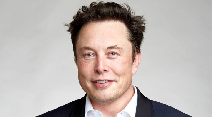 Portrait of a man in a dark blazer and white shirt smiling against a light gray background near-crop headshot