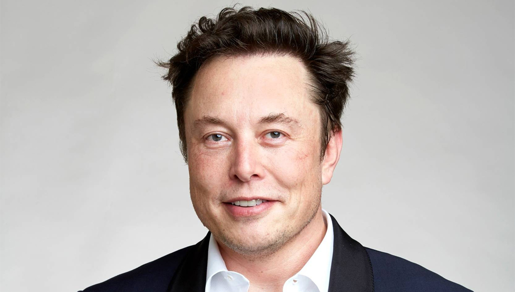 Portrait of a man in a dark blazer and white shirt smiling against a light gray background near-crop headshot